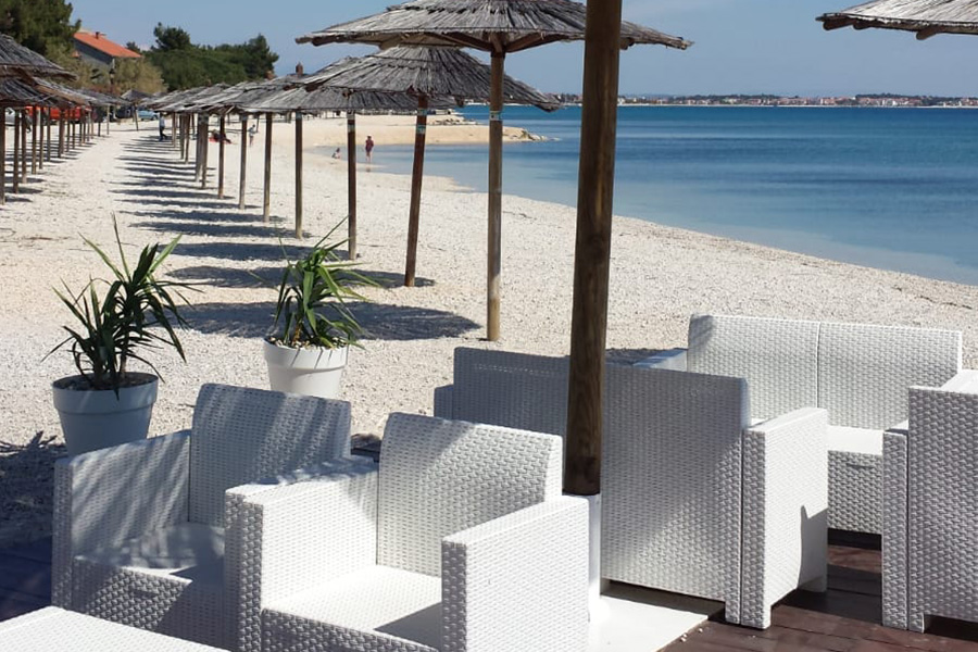 Lounge sjedeća garnitura beach bara uz red suncobrana i plavetnilo mora na otoku Viru
