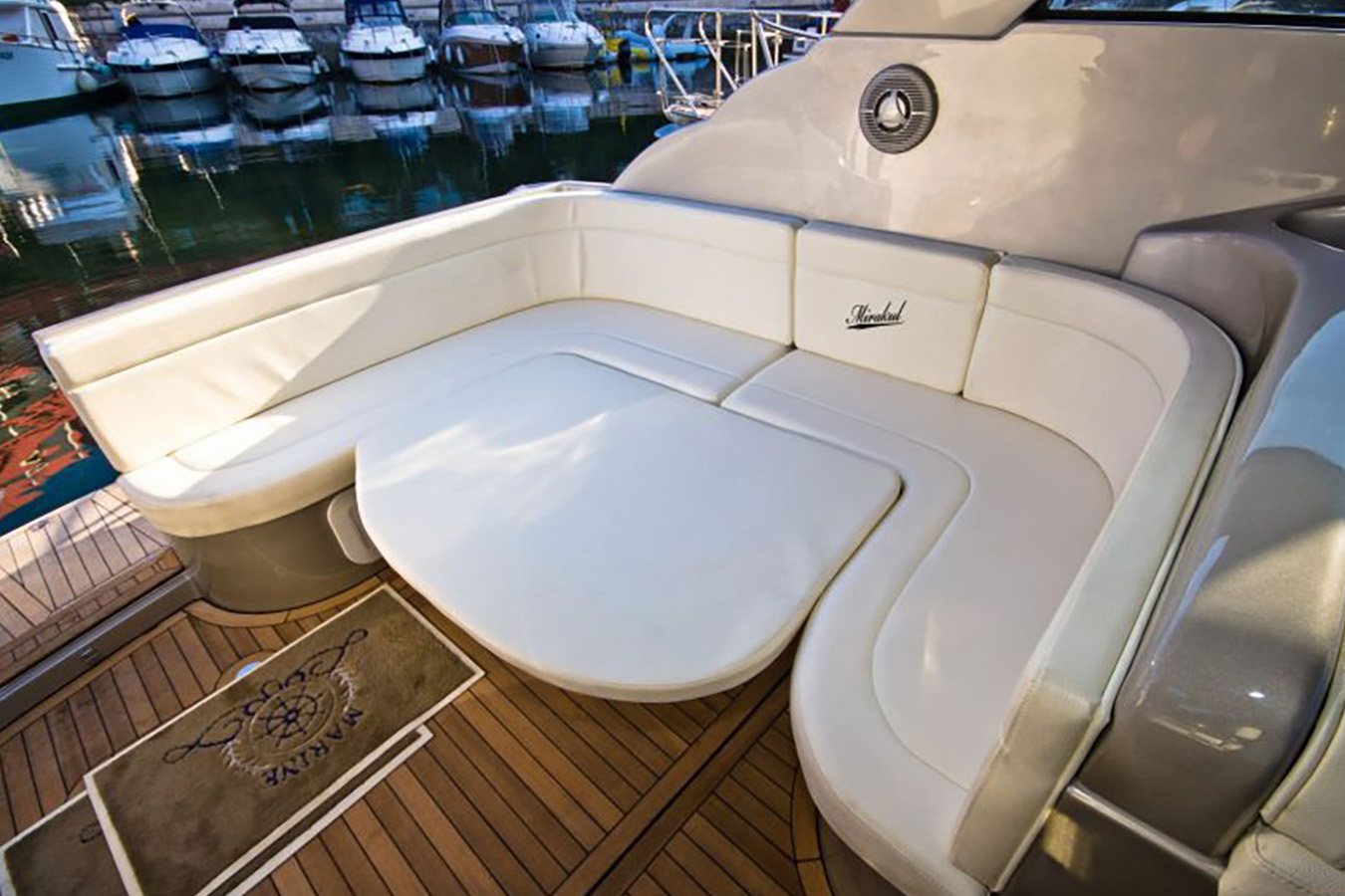 Kokpit jahte Mirakul 30 s udobnim bijelim sjedalima u obliku slova U, stolom za blagovanje i drvenom palubom, s drugim brodovima usidrenim u pozadini