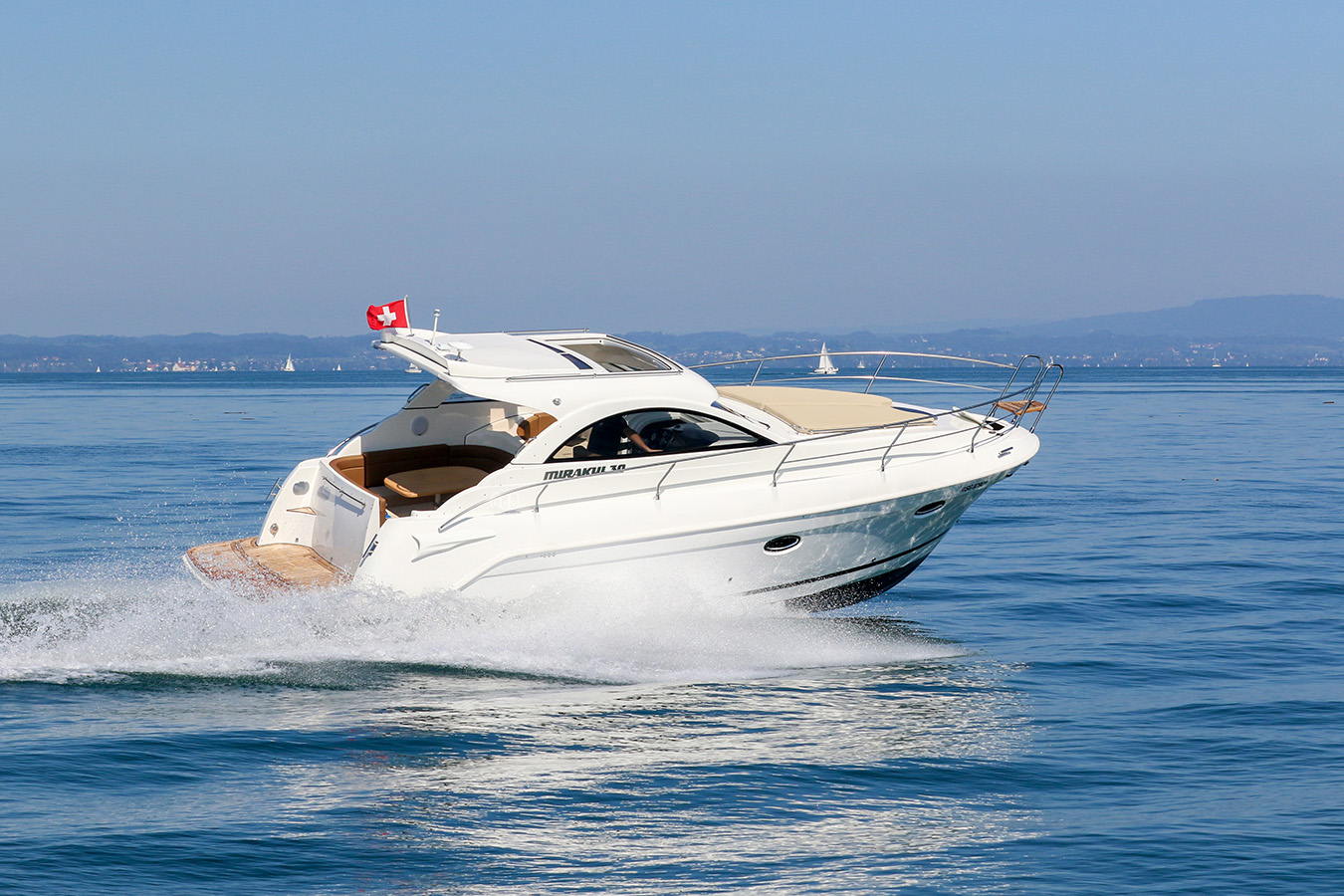 Bijela jahta Mirakul 30 juri preko mirnog plavog mora, ostavljajući pjenušav bijeli trag, pod vedrim nebom sa švicarskom zastavom na krmi