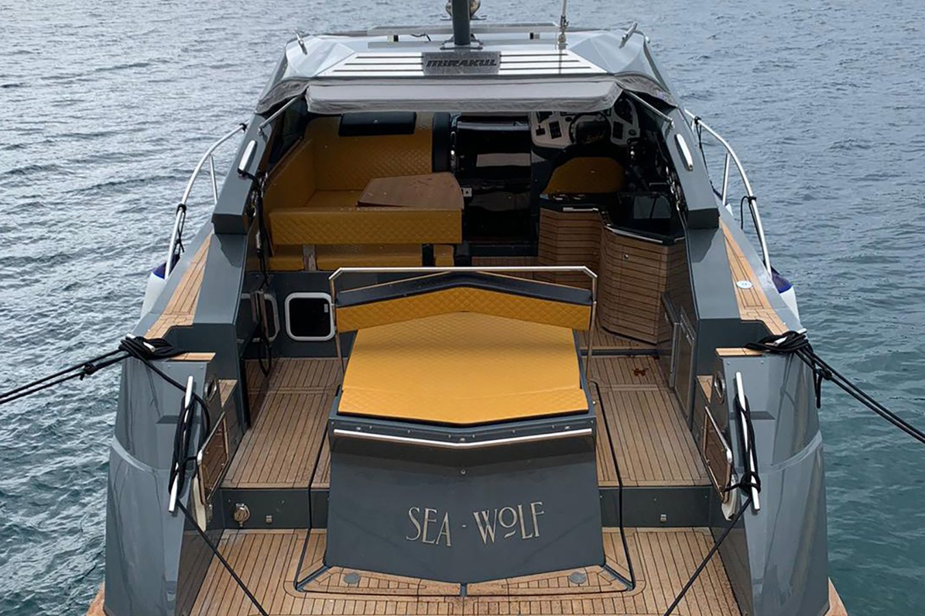 Krmeni pogled na Mirakul 40 privezan uz ponton: velika teak platforma, sklopivi sunčališni modul s jastucima i kokpit s barom desno