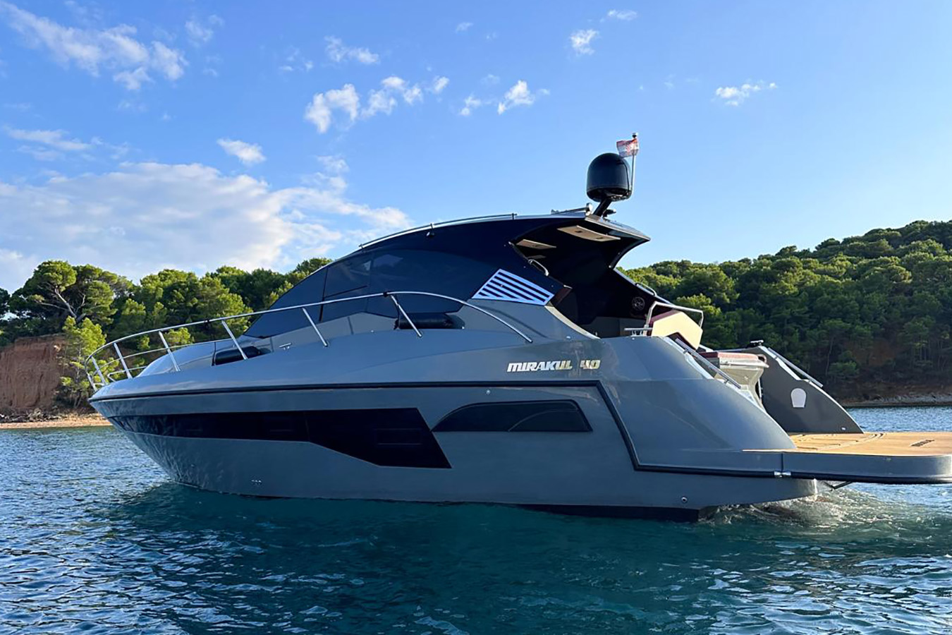 luksuzna jahta na sidru u mirnoj uvali; crni hard-top, prepoznatljiva bočna grafika i izvučena kupališna platforma tik iznad površine mora