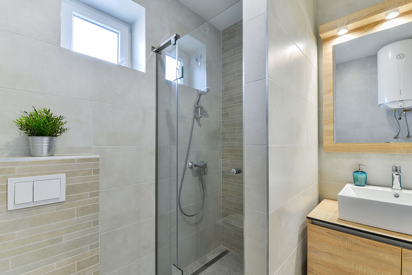 Svjetla, moderna kupaonica u sklopu luksuznog smještaja, s walk-in tušem sa staklenim vratima, četvrtastim bijelim umivaonikom na drvenoj komodi i ogledalom s ugrađenom rasvjetom