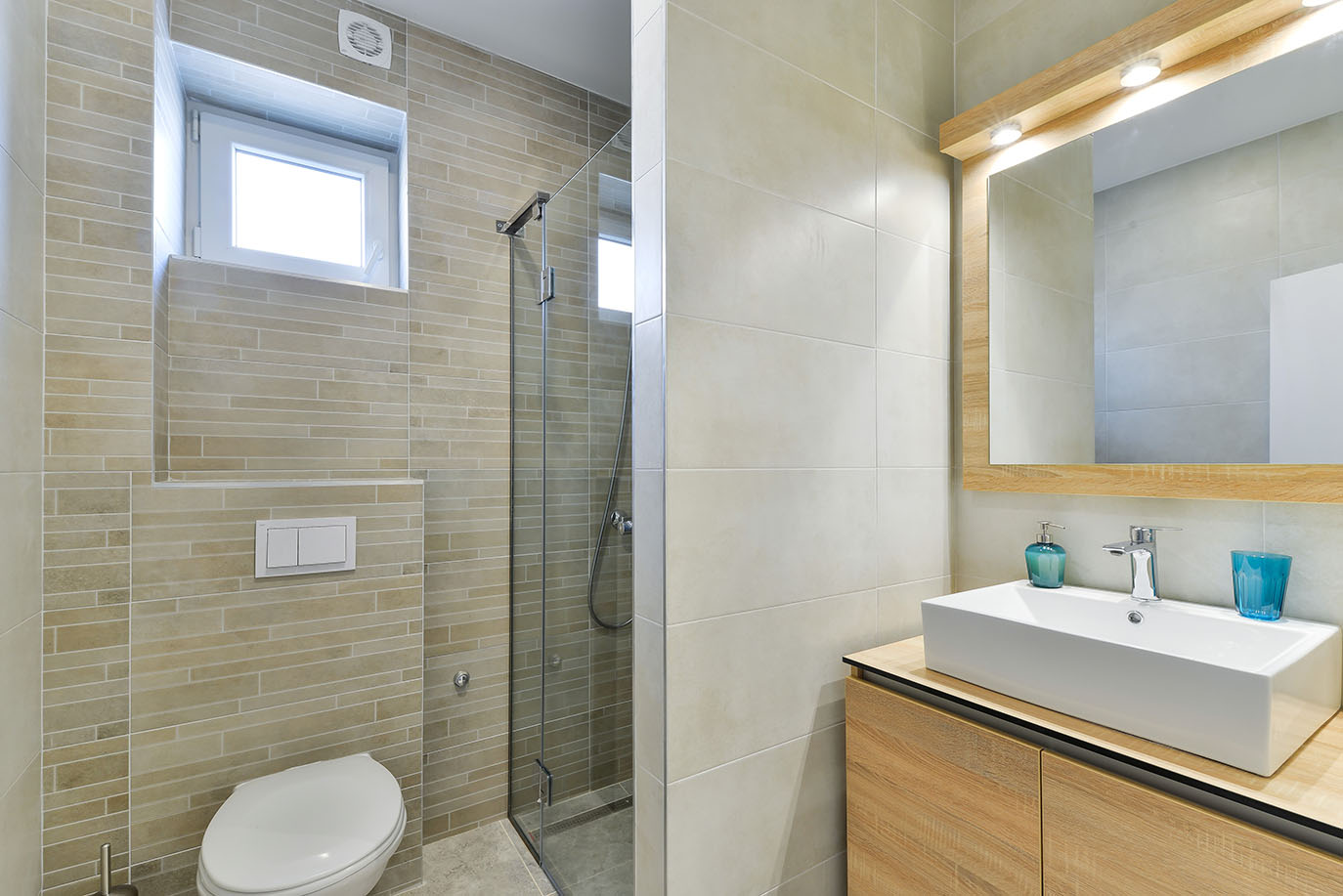 Moderna kupaonica u jednom od apartmanu A2 Resorta Mirakul na otoku Viru, sa svijetlim pločicama, drvenim ormarićem s bijelim umivaonikom, WC školjkom i tuš kabinom sa staklenom pregradom