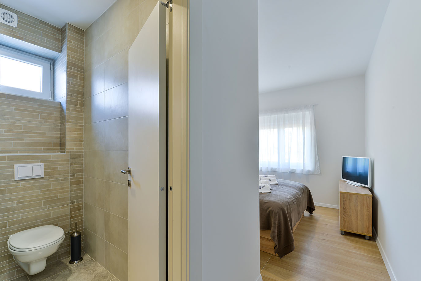 Svijetla, moderna kupaonica s WC-om i pogled na spavaću sobu s udobnim krevetom, prikazujući kvalitetu luksuznog smještaja