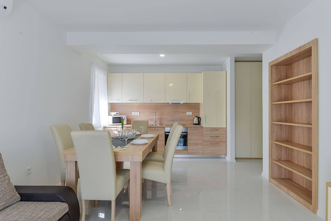 Moderna kuhinja i blagovaonica, idealna za luksuzni smještaj, s drvenim stolom, krem stolicama i elegantnim kuhinjskim elementima