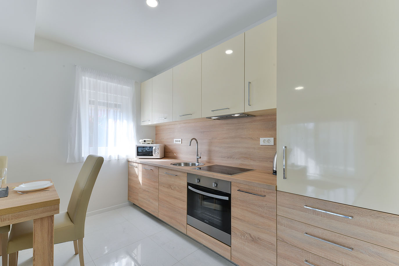 Svijetla, moderna kuhinja sa svijetlim drvenim donjim ormarićima, krem gornjim ormarićima i ugradbenim aparatima, idealna za apartmane Vir