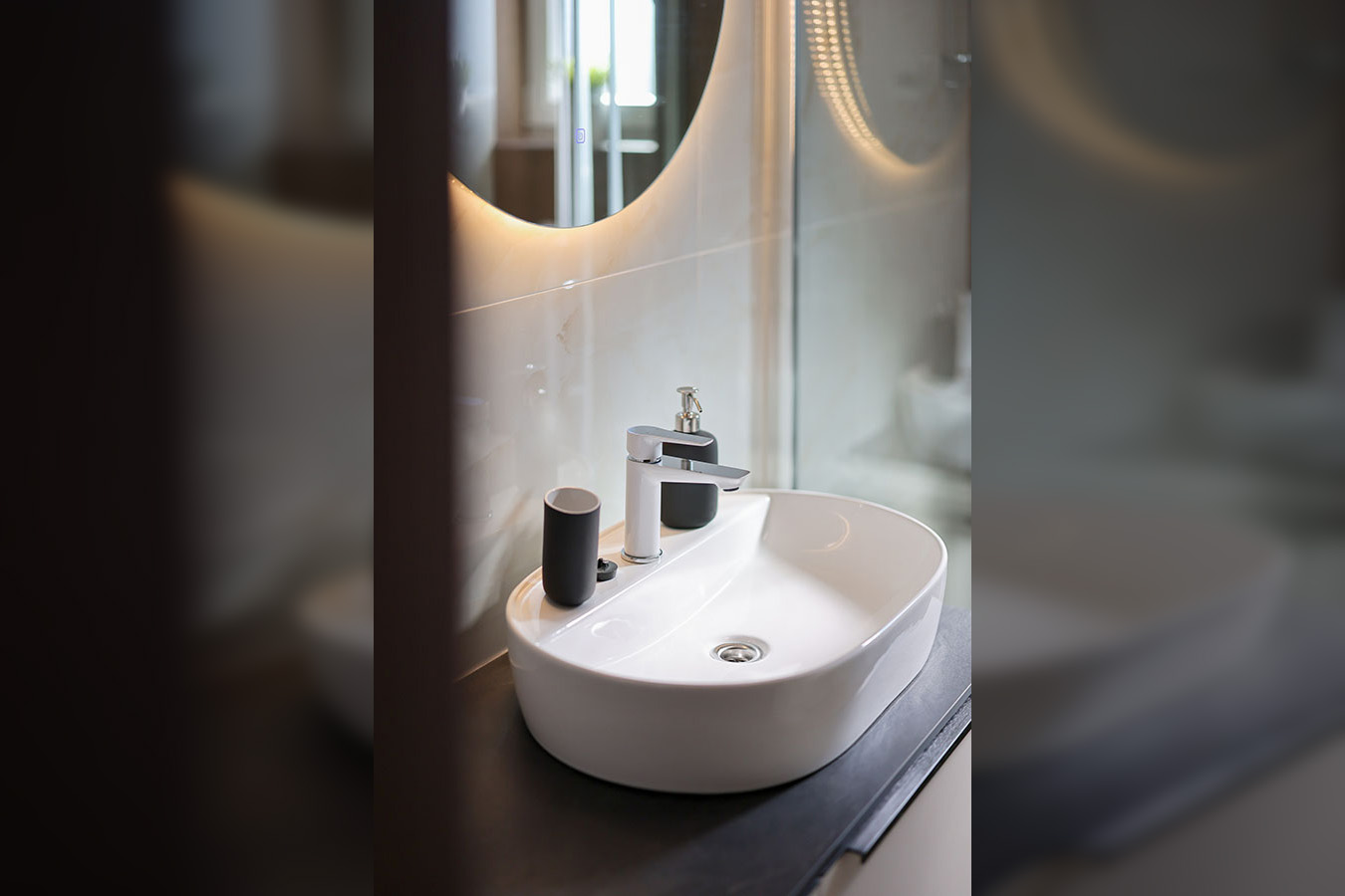 Moderna kupaonica s ovalnim nadgradnim umivaonikom, kromiranom slavinom i osvijetljenim ogledalom, tipična za luksuzni smještaj