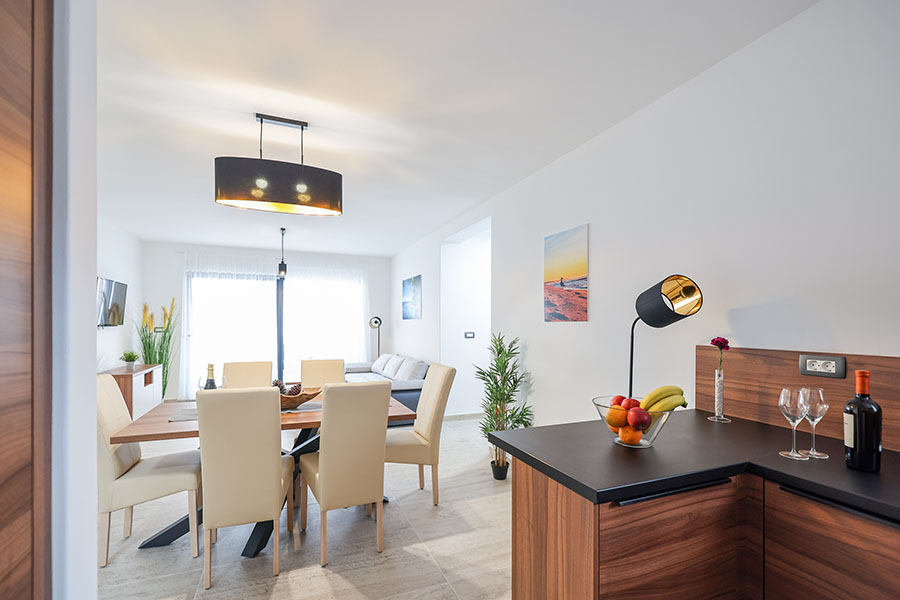 Elegantan otvoreni dnevni boravak i blagovaonica s modernim uređenjem, drvenim stolom za ručavanje, bež stolicama i elegantnim crnim lusterom, koji prikazuje luksuzni smještaj