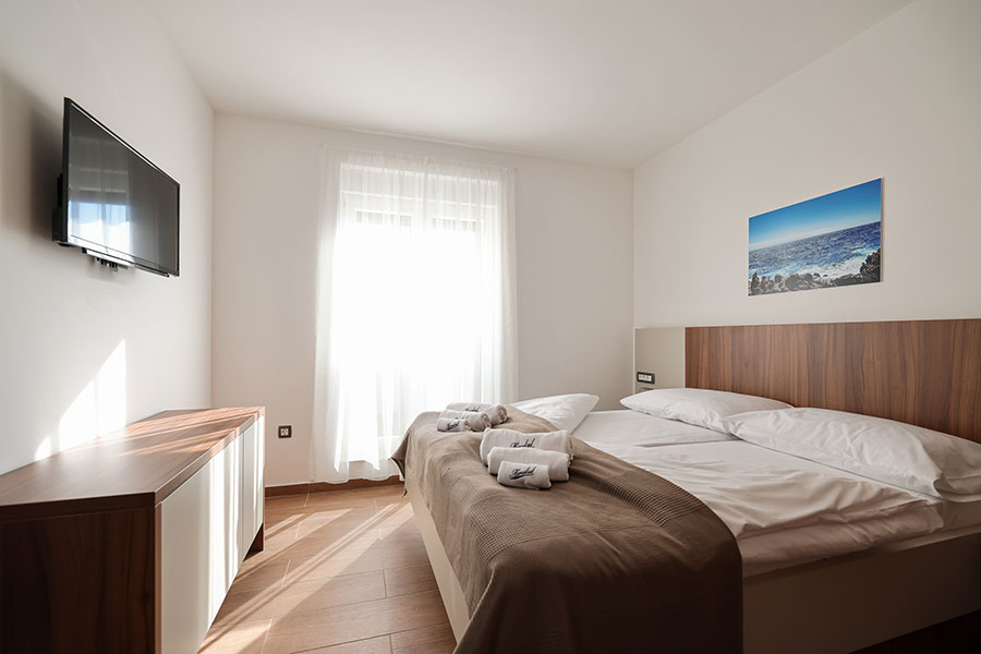 Svijetla i moderna spavaća soba s udobnim bračnim krevetom, drvenim namještajem i zidnim TV-om, idealna za apartmane Vir