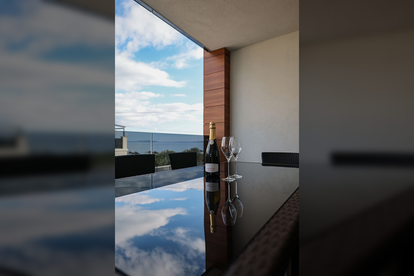 Boca pjenušca i dvije čaše na reflektirajućem stolu na balkonu s pogledom na more, prikazujući ponudu Resorta Mirakul II