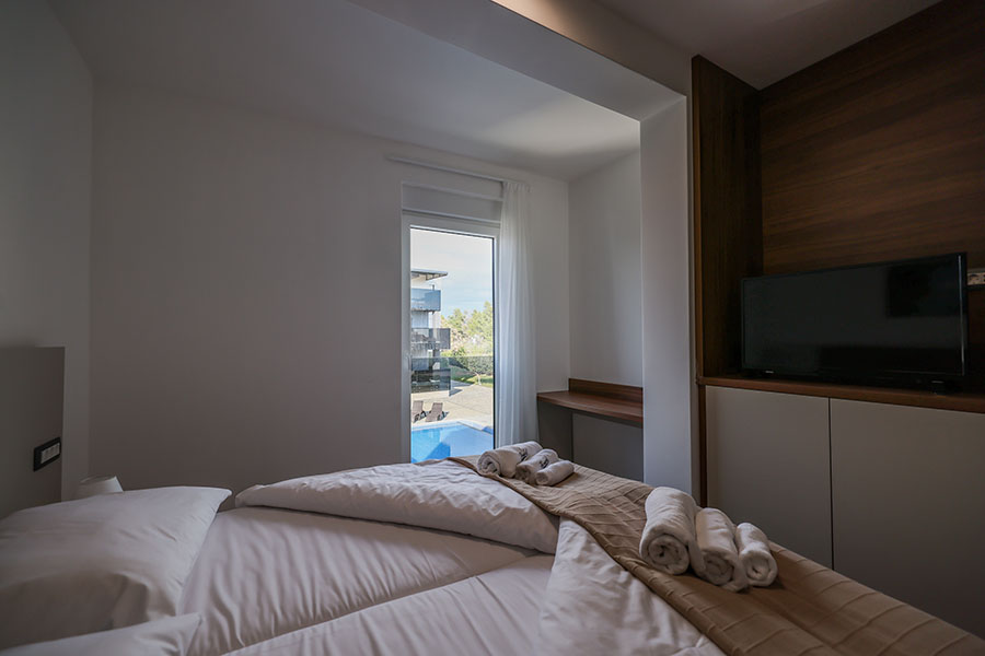 Moderna spavaća soba u luksuznom smještaju, s uredno namještenim krevetom, televizorom i prozorom s pogledom na bazen