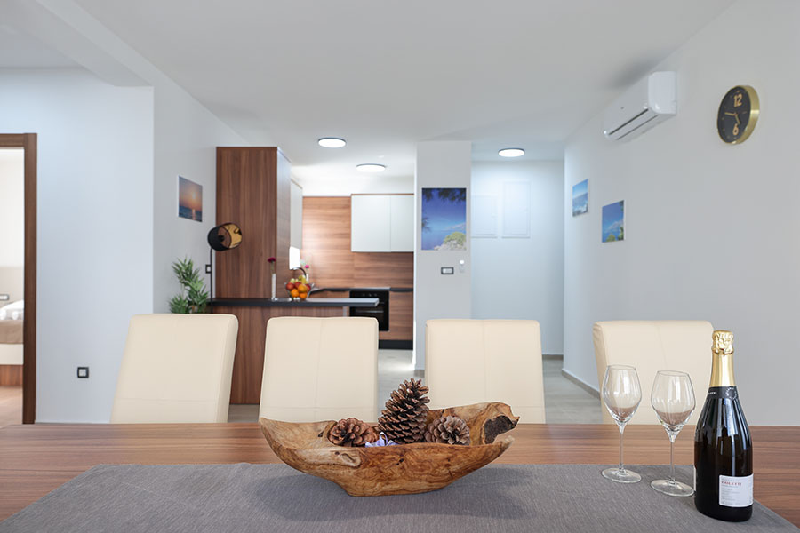 Prostrana i moderna blagovaonica s drvenim stolom, ukrasom od borovih šišarki i šampanjcem, koja vodi u dobro opremljenu kuhinju, idealna za luksuzni smještaj