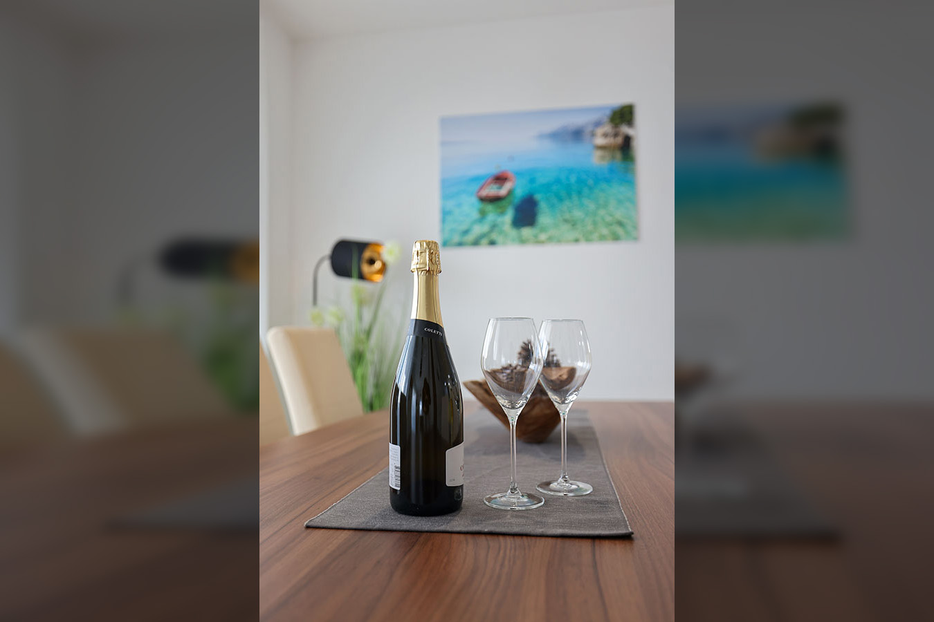 Boca pjenušca i dvije elegantne čaše na drvenom stolu, naglašavajući sofisticirane detalje luksuznog smještaja