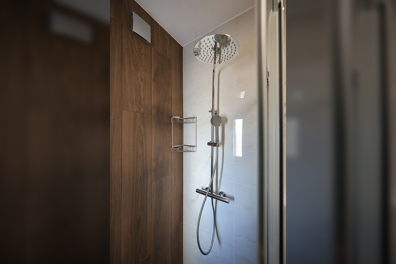 Moderan tuš s kišnom glavom i elegantnim armaturama, uključujući kromiranu policu za odlaganje, prikazuje visoku kvalitetu i udobnost luksuznog smještaja