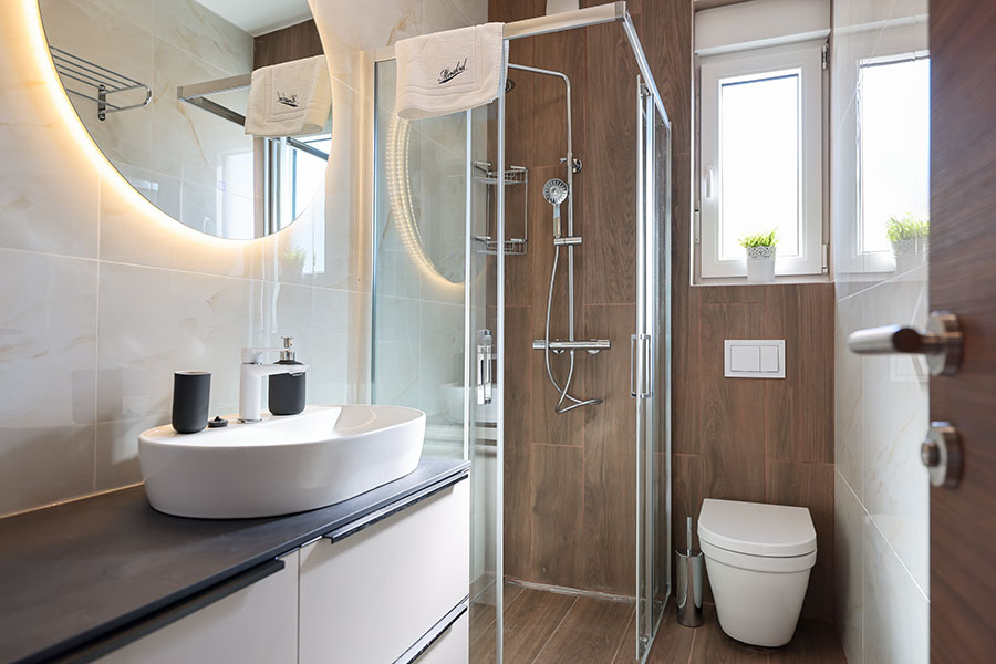 Moderna, dobro osvijetljena kupaonica s elegantnim umivaonikom, velikim okruglim ogledalom s pozadinskim osvjetljenjem, tušem s staklenom kabinom i čistim WC-om, što je obilježje luksuznog smještaja