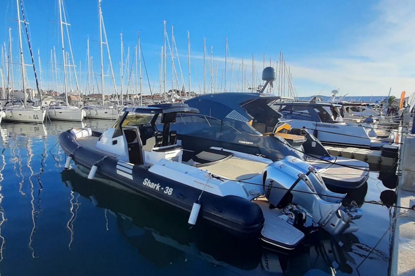 Moderan luksuzni gumenjak s dva snažna Honda izvanbrodska motora usidren je u marini, s brojnim jedrilicama u pozadini po sunčanom danu