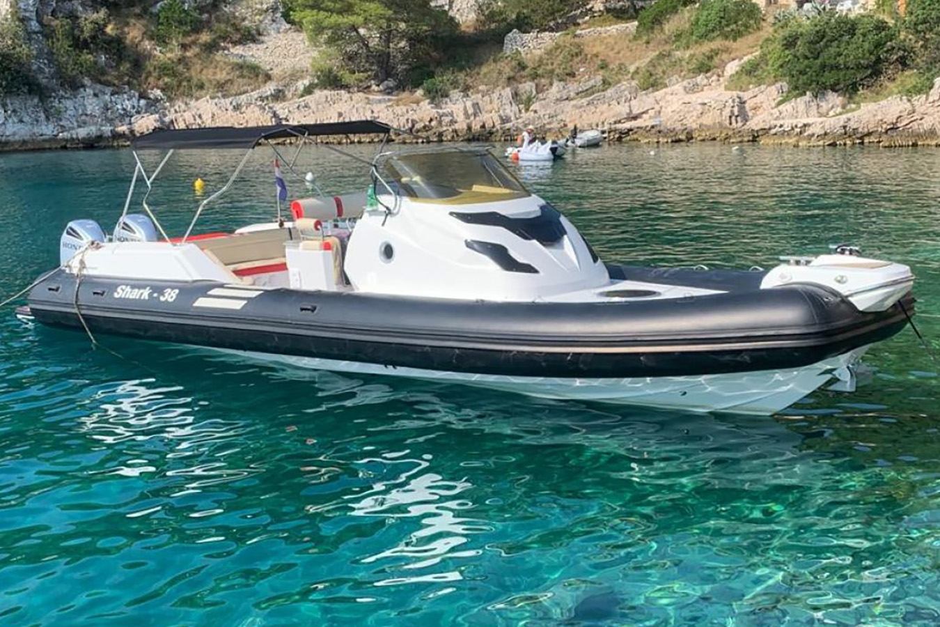 Elegantan bijeli i crni luksuzni gumenjak s dva vanbrodska motora mirno pluta u kristalno čistom tirkiznom moru uz stjenovitu obalu