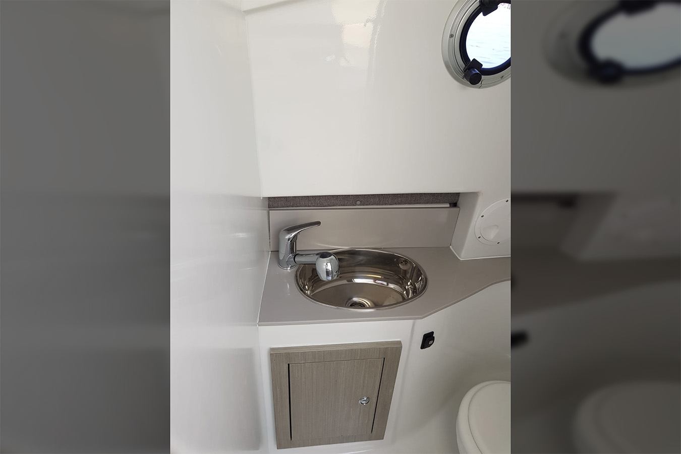 Čist i moderan kupaonski prostor na luksuznom gumenjaku, s inox umivaonikom, kromiranom slavinom i svijetlim drvenim ormarićem ispod