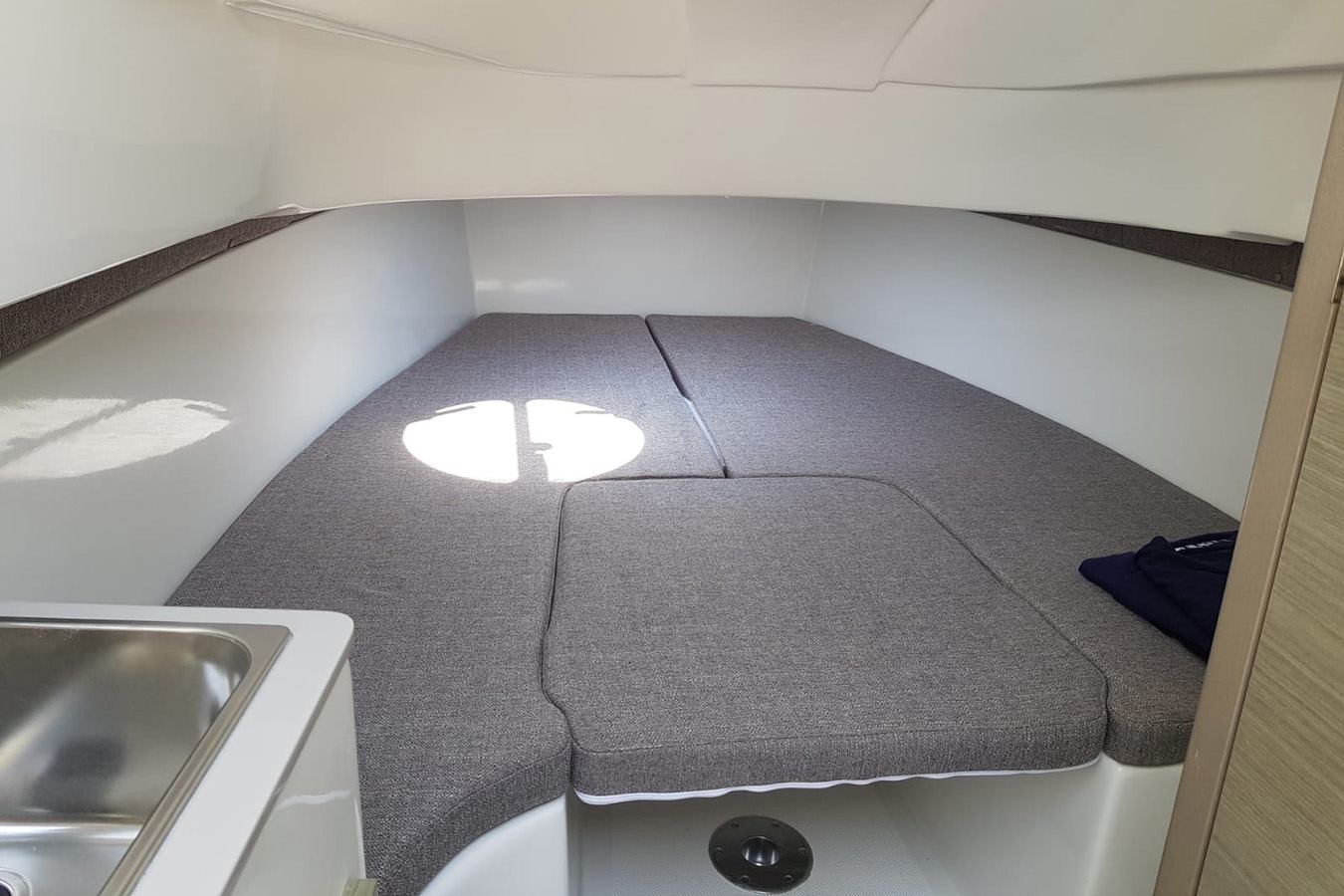 Unutrašnjost kabine luksuznog gumenjaka s udobnim sivim jastucima koji čine V-ležaj, bijelim zidovima i malim sudoperom u prvom planu