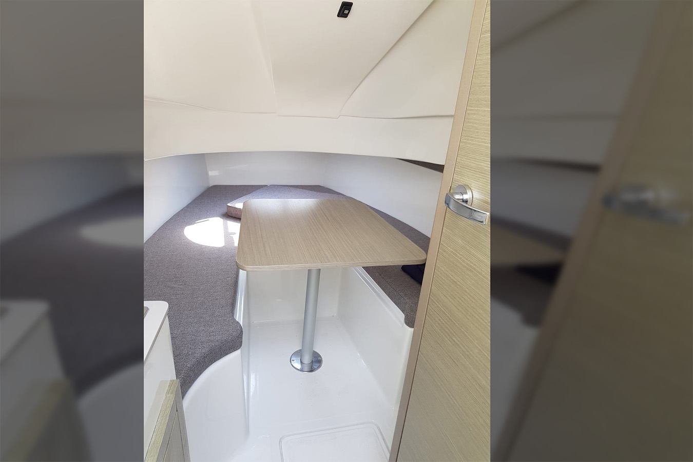 Prostrana i svijetla unutrašnjost kabine plovila Shark 38, s drvenim stolom za blagovanje, udobnim sivim tapeciranim sjedalima i čistim bijelim završecima