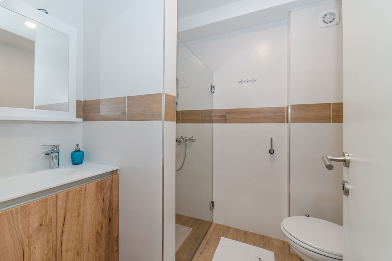 Prekrasno uređena kupaonica s elegantnim drvenim ormarićem, prostranim walk-in tušem i modernim armaturama, karakteristična za luksuzne apartmane u Hrvatskoj