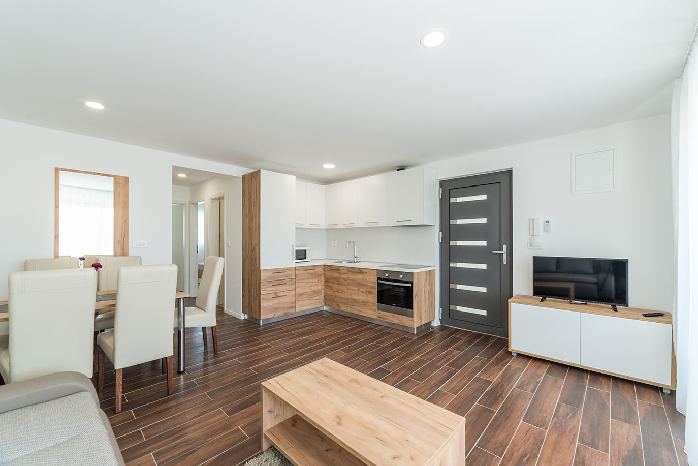 Prostrani otvoreni dnevni boravak modernog apartmana za odmor na Viru, s blagovaonskim stolom i stolicama, potpuno opremljenom kuhinjom s drvenim detaljima te dnevnim dijelom s TV-om i stolićem