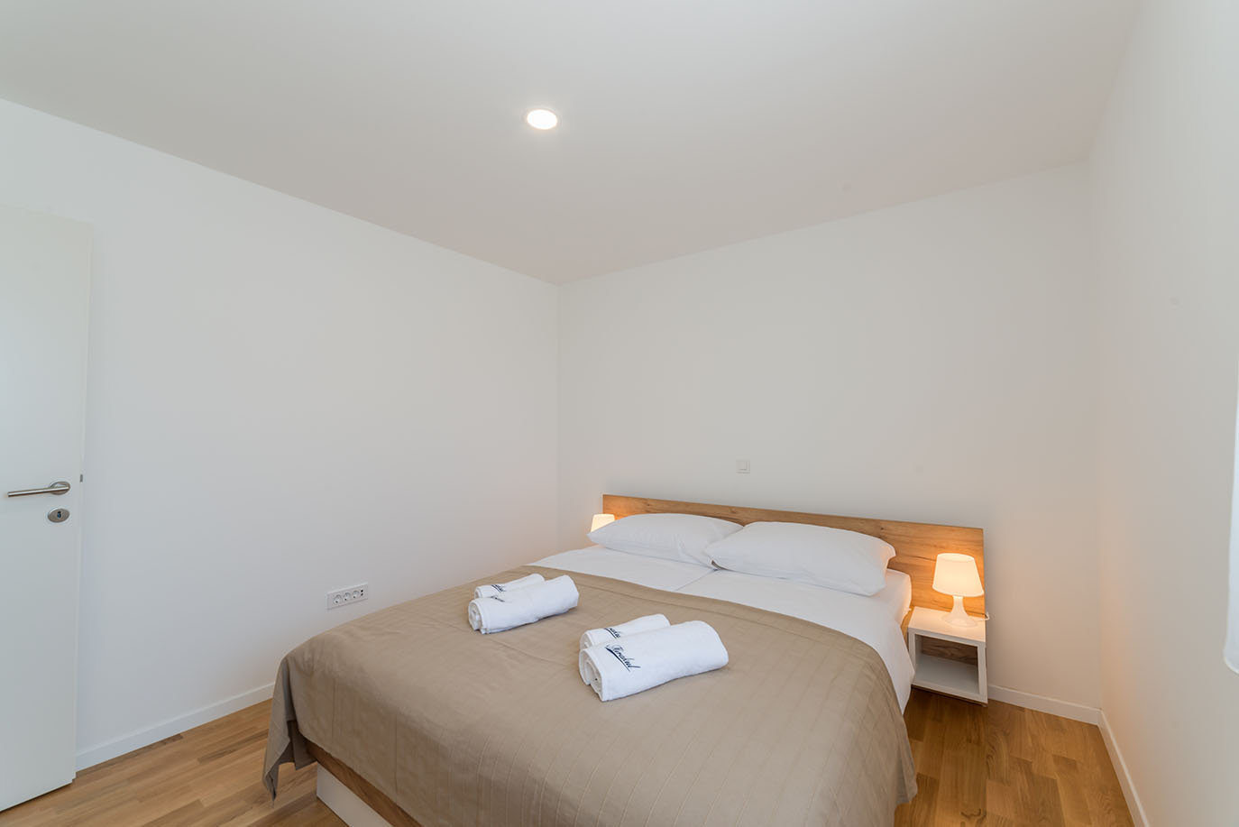 Čista i moderna spavaća soba u apartmanima Villa Mirakul, s udobnim bračnim krevetom, svježom bijelom posteljinom, ručnicima i toplim noćnim svjetiljkama