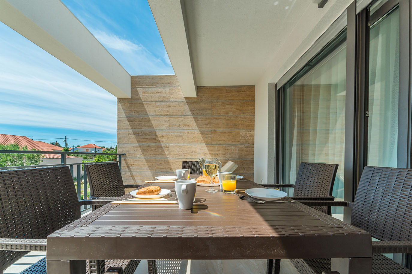 Sunčani balkon apartmana za odmor na Viru s postavljenim doručkom i pletenim stolicama, pružajući ugodan prostor za objedovanje na otvorenom