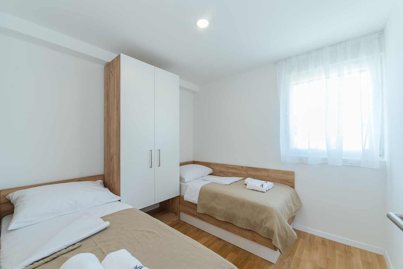 Čista i svijetla spavaća soba s dva odvojena kreveta i modernim ormarom, primjer udobnih smještajnih jedinica u apartmanima Villa Mirakul