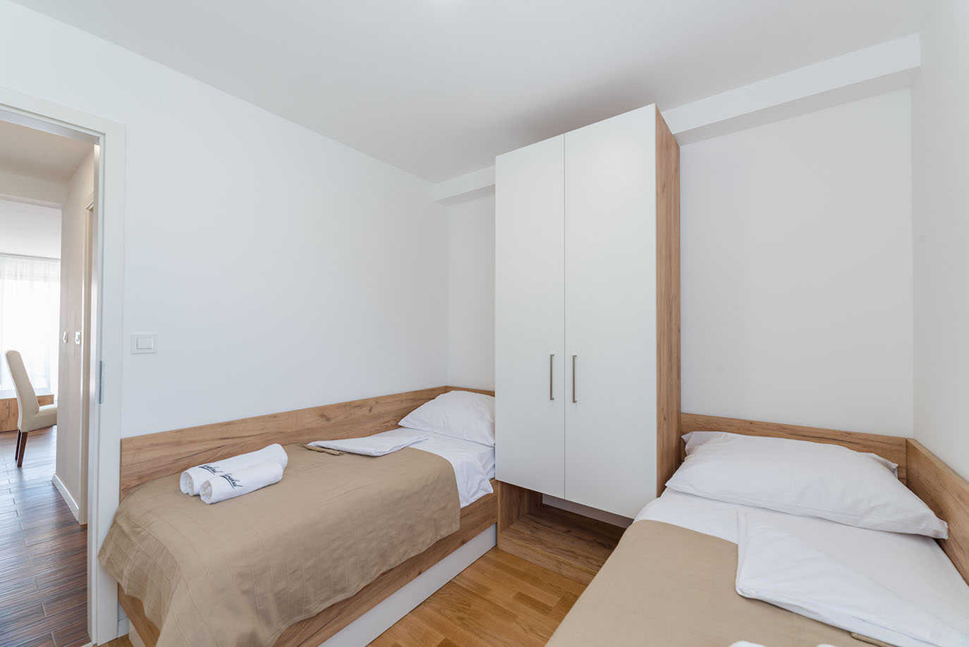Svijetla, minimalistička spavaća soba u apartmanima za odmor Vir s dva kreveta za jednu osobu, bijelim i svijetlim drvenim ormarom te toplim drvenim podovima