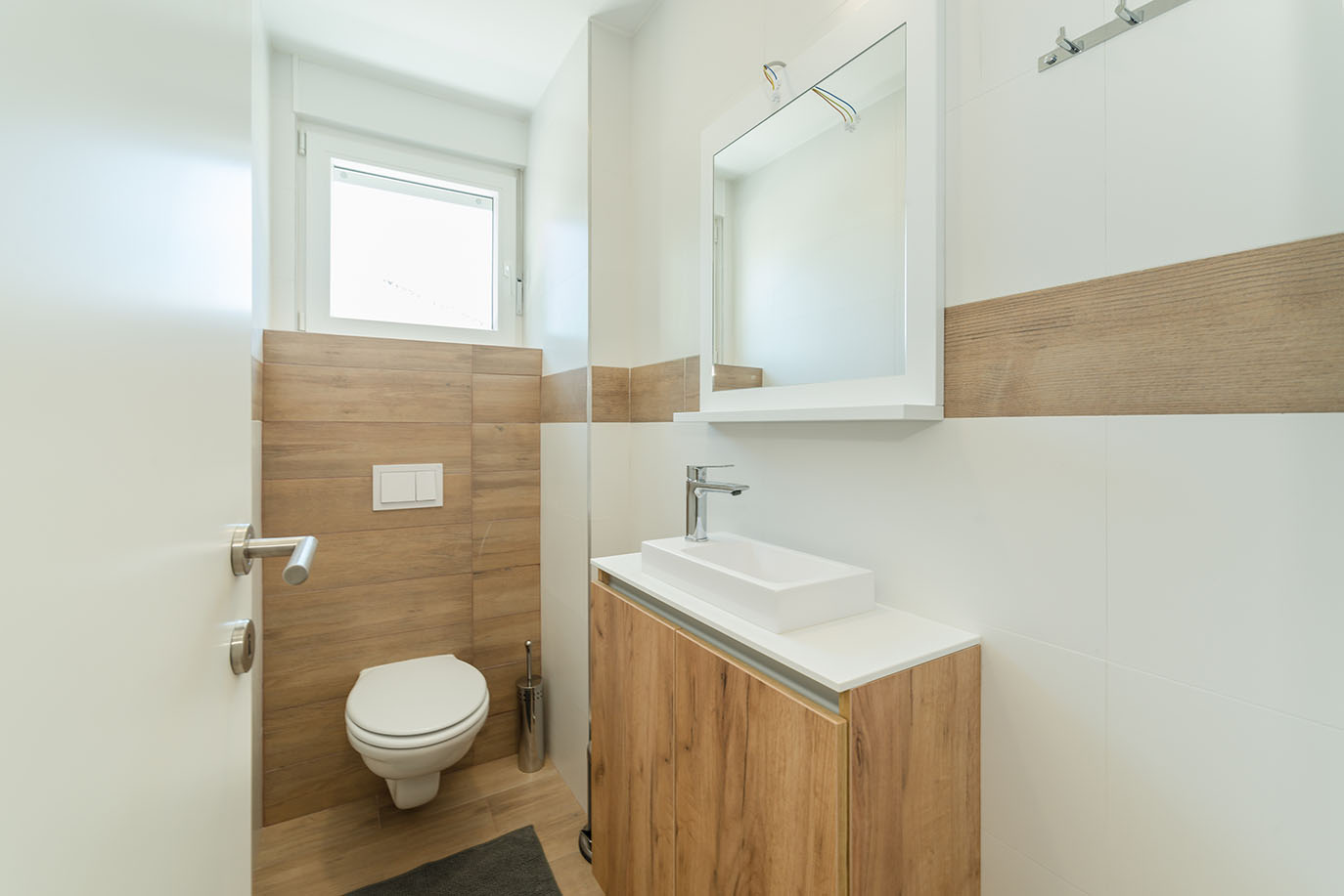 Moderna kupaonica s drvenim i bijelim pločicama, visećim WC-om i ormarićem s pravokutnim umivaonikom, tipična za apartmane Vir