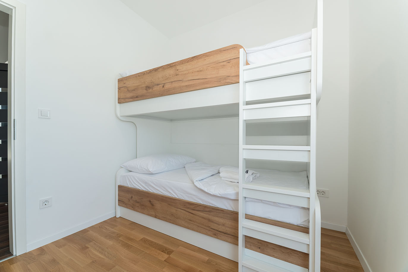 Svjetla i moderna spavaća soba s bijelim krevetima na kat i drvenim detaljima, idealna za goste u apartmanima Vir