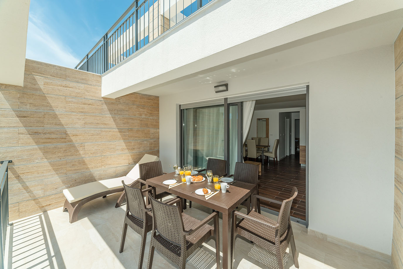 Svijetla vanjska terasa s blagovaonskim stolom postavljenim za doručak i ležaljkom, savršena za goste koji borave u apartmani Vir