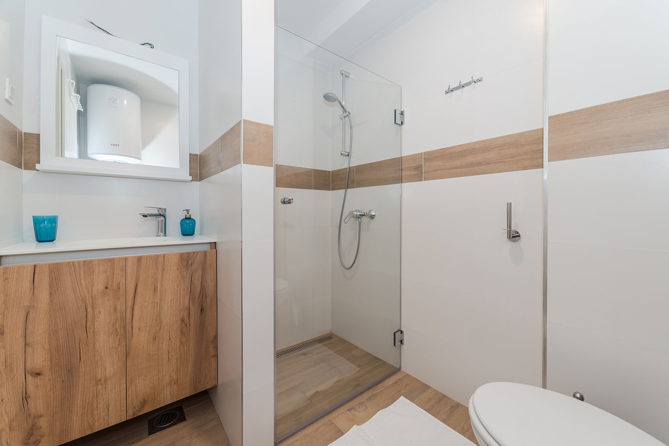 Svijetla i moderna kupaonica s drvenim kupaonskim elementom, elegantnim umivaonikom, ogledalom, staklenom tuš kabinom i WC-om, savršena za goste u apartmanima Vir