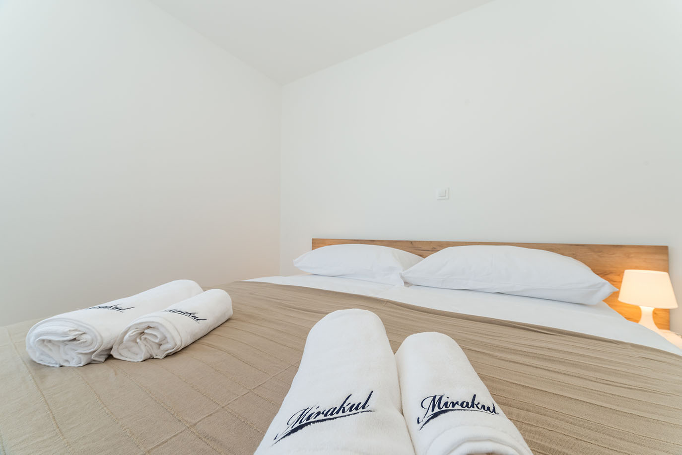 Svijetla i moderna spavaća soba s udobnim krevetom, bijelim jastucima i brendiranim ručnicima, idealna za goste apartmana Vir