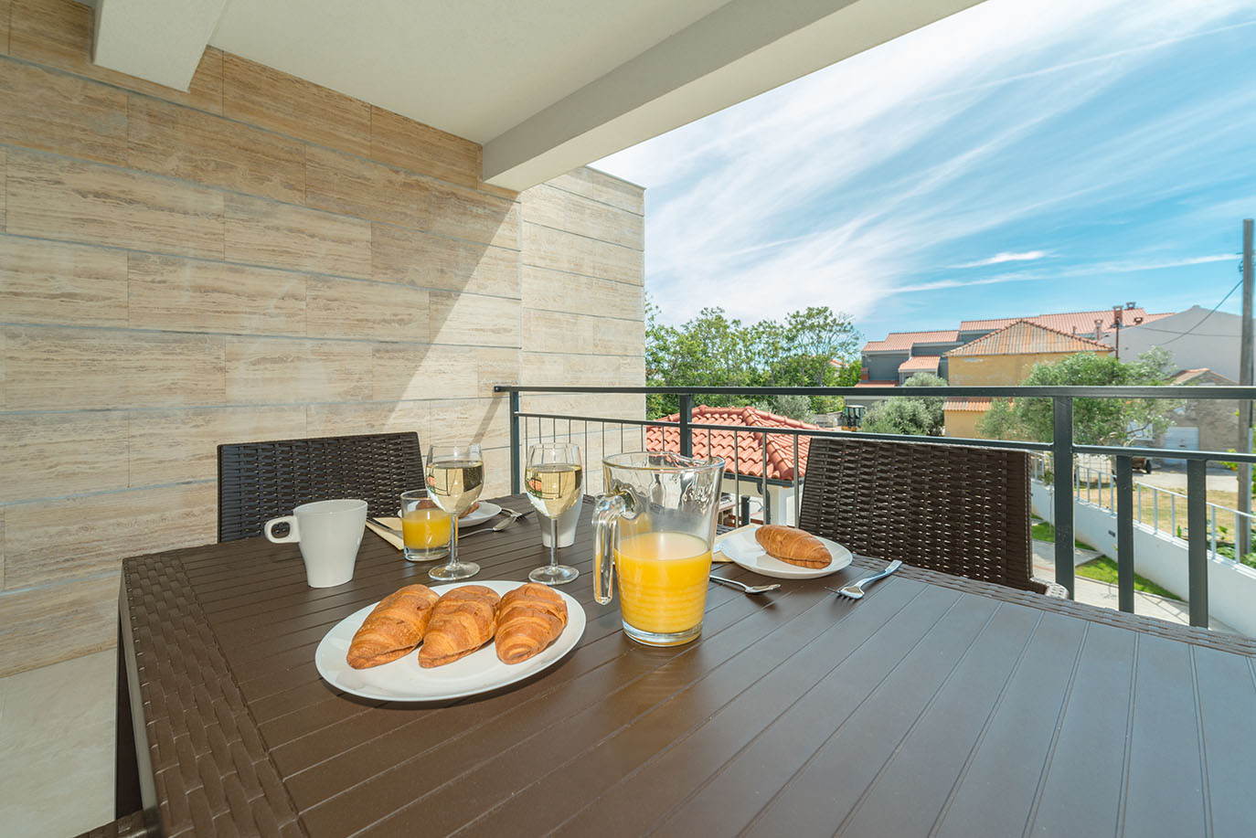 Ukusni doručak s kroasanima, sokom od naranče i vinom poslužen na sunčanom balkonu, s prekrasnim pogledom na krovove i zelenilo, idealan za goste apartmani Vir