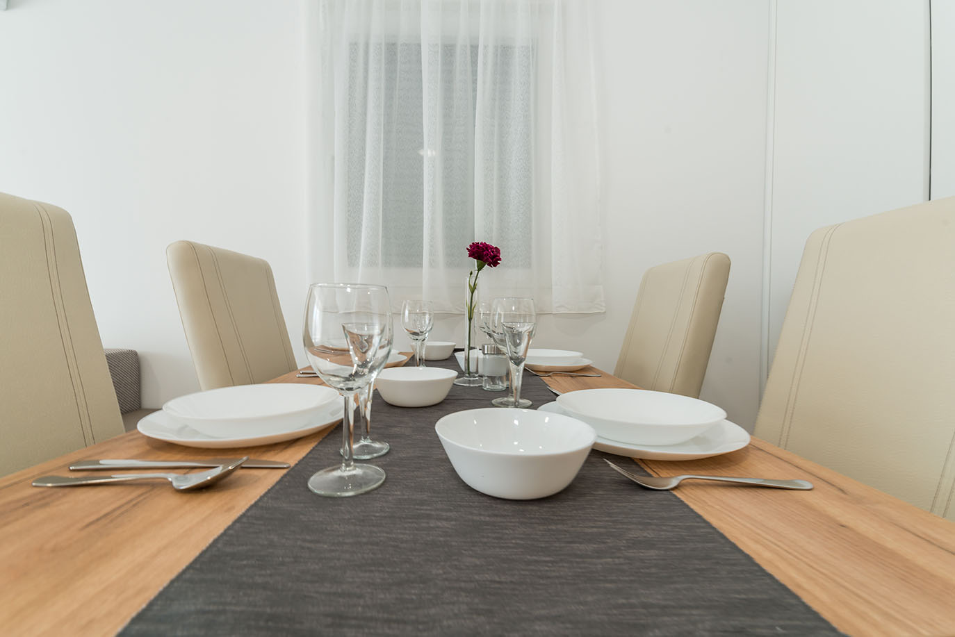 Elegantno postavljen blagovaonski stol s bijelim posuđem, čašama i jednim crvenim cvijetom, prikazujući udoban interijer Villa Mirakul