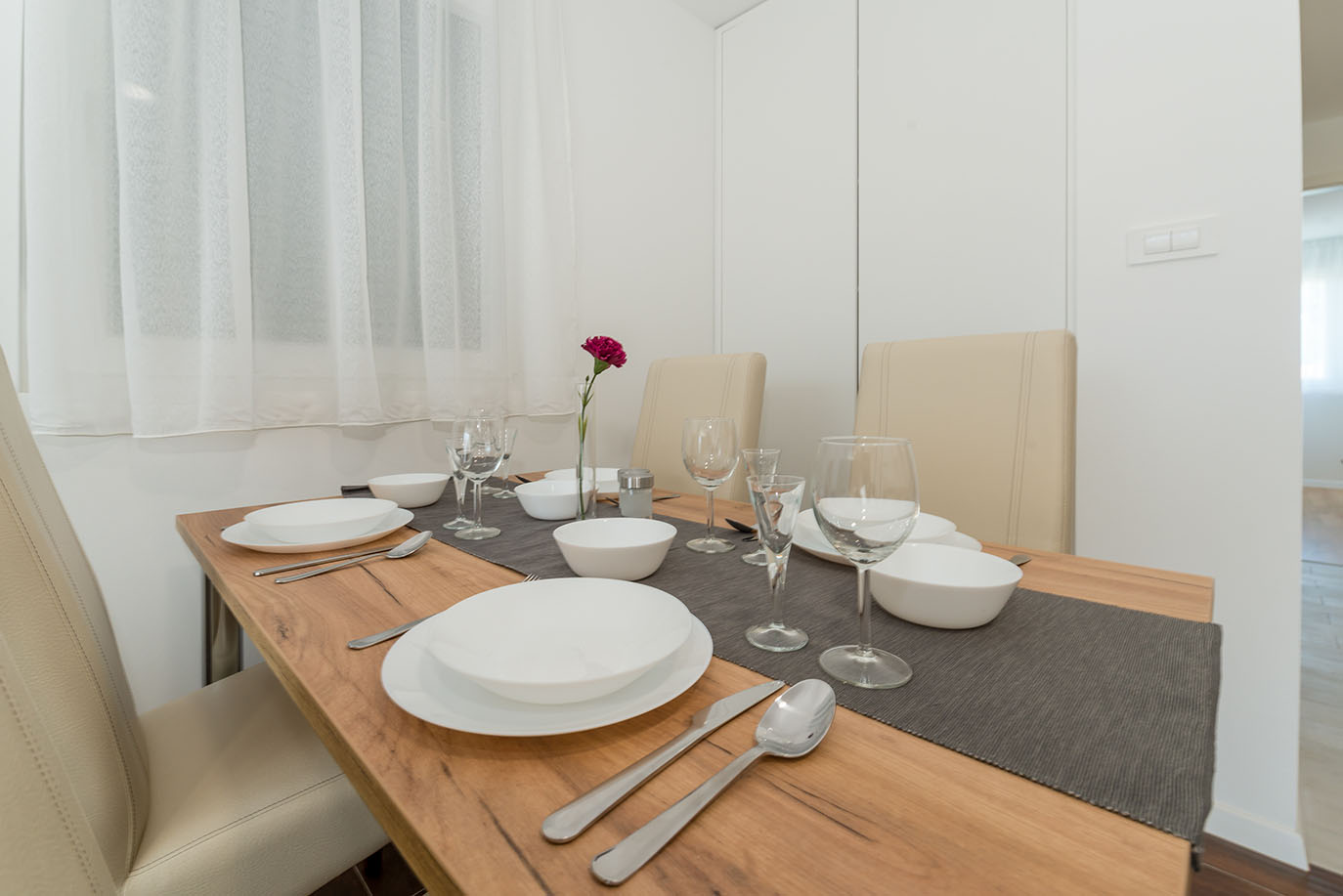 Moderan stol za blagovanje postavljen bijelim posuđem, čašama i ukrasnim cvijetom, naglašavajući ugodnu atmosferu u Villi Mirakul