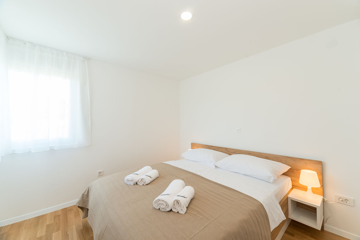 Svijetla i čista spavaća soba s bračnim krevetom, drvenim uzglavljem, bijelom posteljinom i smotanim ručnicima, tipična za kvalitetne apartmane Vir