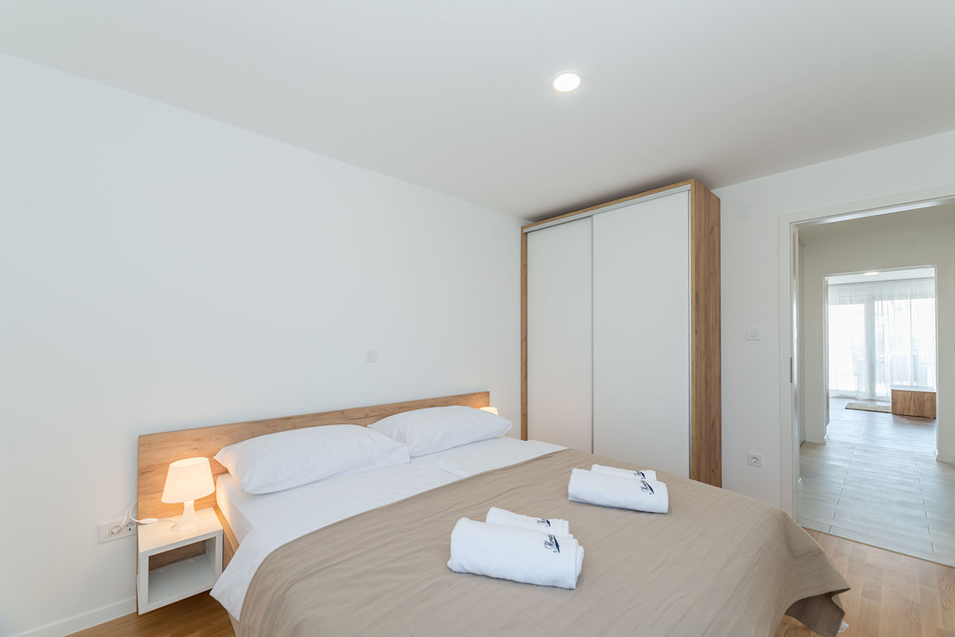 Svijetla i moderna spavaća soba u Villi Mirakul, s udobnim krevetom, bijelom posteljinom i uredno složenim ručnicima, drvenim uzglavljem te ugradbenim ormarom