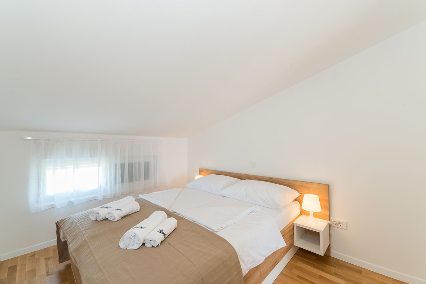 Svijetla i moderna spavaća soba u Villi Mirakul s velikim krevetom, bijelom posteljinom, drvenim uzglavljem i ukrasnim ručnicima