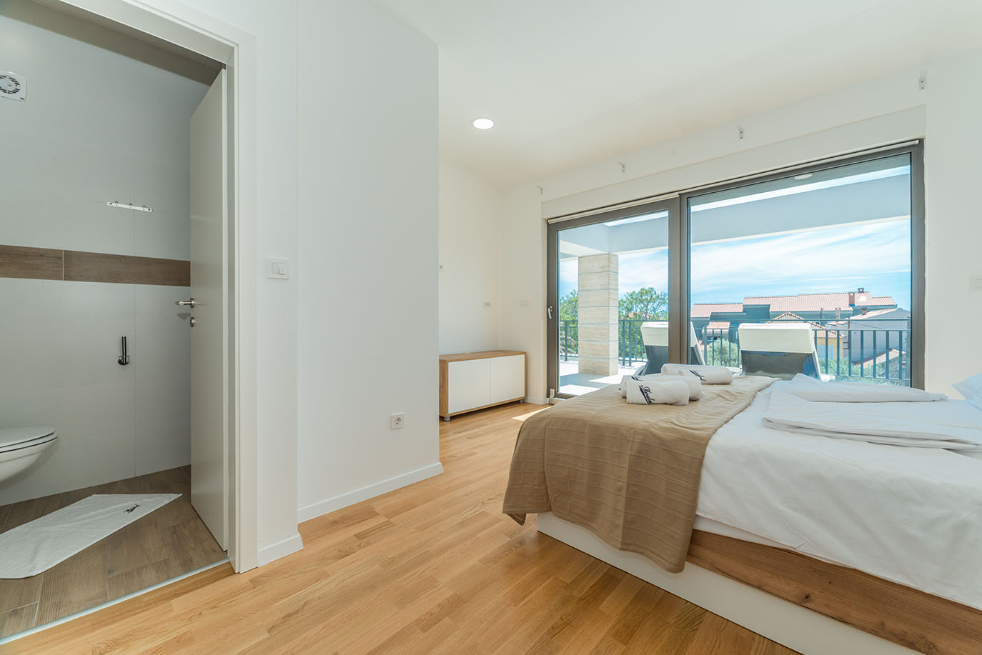 Moderna spavaća soba s velikim krevetom, drvenim podom i privatnim balkonom s pogledom na grad, uobičajena za apartmane Vir